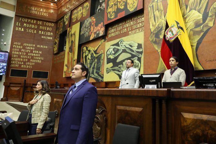 Curules del CAL de la Asamblea Nacional donde se observa al presidente Virgilio Saquisela delante de la bandera de Ecuador.